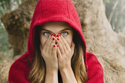 Verängstigte Frau mit roter Kapuze, die ihr Gesicht mit den Händen bedeckt - GEMF000173