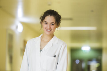 Porträt eines lächelnden jungen Arztes auf dem Boden eines Krankenhauses - DISF001612