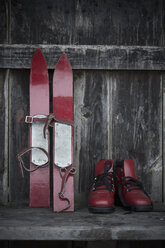 Ein Paar rote Kinderskier und rote Skischuhe auf einer alten Holzbank - ASF005549
