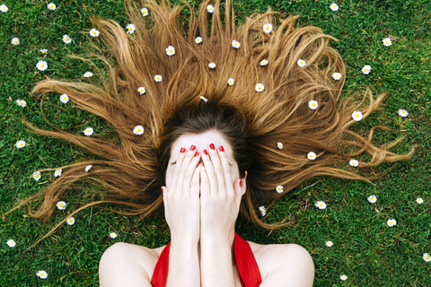 Woman lying on grass in spring with hands on face and flowers on hair stock photo