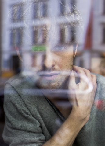 Junger Mann schaut durch eine Fensterscheibe, lizenzfreies Stockfoto