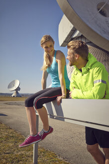 Germany, Raisting, young jogger couple having a rest at ground station - KDF000713