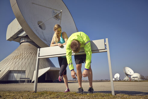 Germany, Raisting, young jogger couple having a rest at ground station - KDF000714