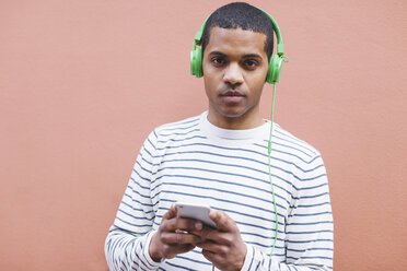 Porträt eines jungen Mannes, der mit grünen Kopfhörern Musik hört - EBSF000568