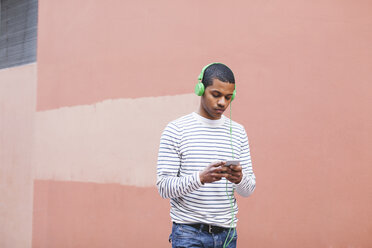 Junger Mann hört Musik mit grünen Kopfhörern - EBSF000569