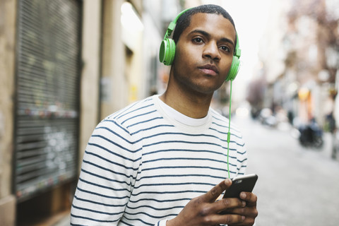 Spain, Barcelona, portrait of young man hearing music with green headphones on street stock photo