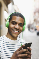 Portrait of smiling young man hearing music with green headphones on street - EBSF000576