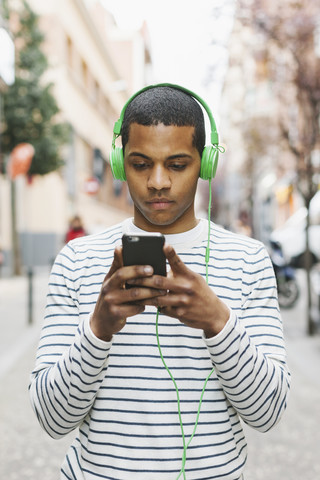 Spanien, Barcelona, junger Mann hört Musik mit grünen Kopfhörern auf der Straße, lizenzfreies Stockfoto