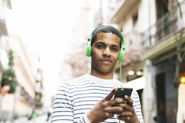 Spain, Barcelona, portrait of smiling young man hearing music with green headphones on street - EBSF000578