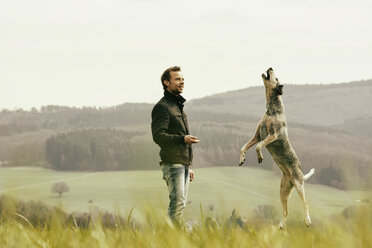 Man exercising with dog on meadow - ONF000810