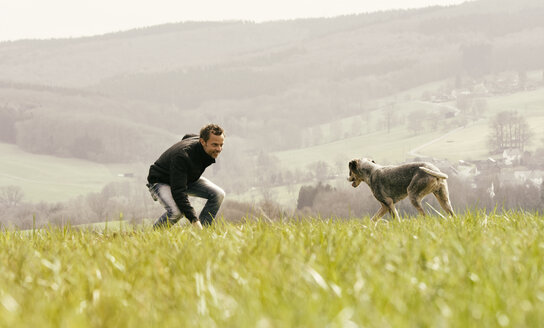 Mann beim Sport mit Hund auf einer Wiese - ONF000813