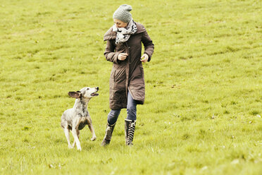 Woman running with dog on meadow - ONF000818