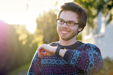 Porträt eines lächelnden jungen Hipsters mit Smartwatch im Gegenlicht - BRF001198