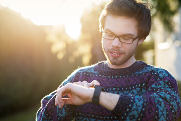 Porträt eines jungen Hipsters mit Smartwatch im Gegenlicht - BRF001186