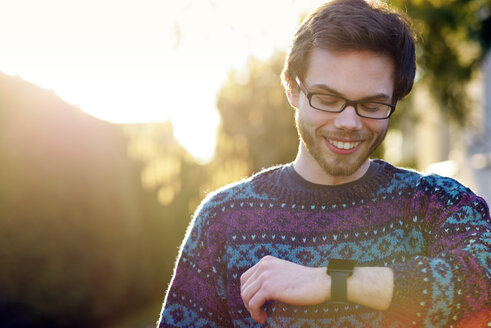 Porträt eines lächelnden jungen Hipsters, der auf seine Smartwatch schaut - BRF001187