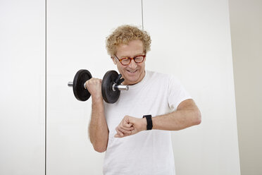 Senior man training with dumbells using smartwatch - RHF000787