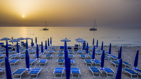 Italien, Sizilien, Cefalu, Blick auf Sonnenschirm und Liegestühle am Meer in der Abenddämmerung, lizenzfreies Stockfoto