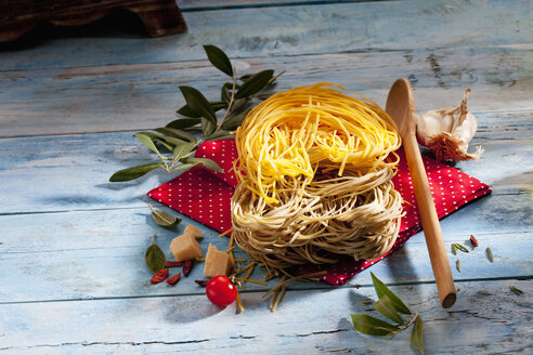 Zwei Sorten ungekochte Tagliolini-Nudeln, Parmesan, Chilischoten, Kräuter, Olivenzweig und Kochlöffel - CSF025301