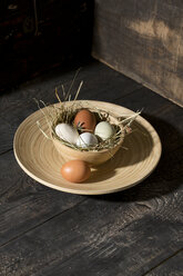 Easter nest with eggs in bowl on dark wood - MAEF010244