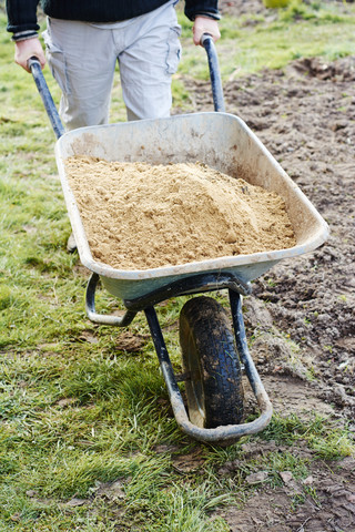 Mann transportiert Sand in einer Schubkarre, lizenzfreies Stockfoto