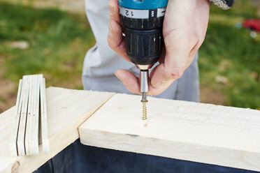 Gärtner schraubt Holzbohlen an, um ein Hochbeet zu bauen - HAW000776