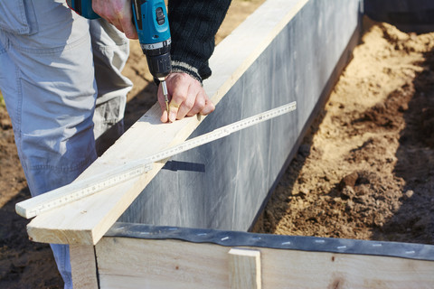 Gärtner schraubt Holzbohlen an, um ein Hochbeet zu bauen, lizenzfreies Stockfoto
