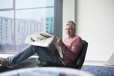Man sitting in a leather chair reading newspaper - RBF002613