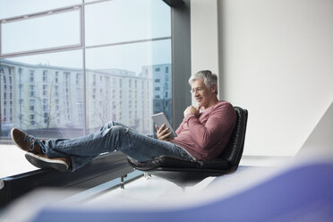 Mann sitzt in einem Ledersessel und benutzt ein digitales Tablet - RBF002614