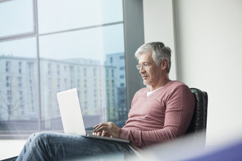 Mann sitzt in einem Ledersessel und benutzt einen Laptop - RBF002616