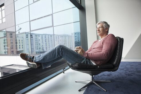 Mann mit Kaffeetasse entspannt sich in einem Ledersessel zu Hause - RBF002617
