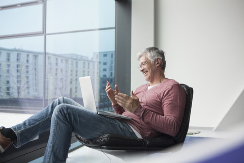 Mann in einem Ledersessel sitzend und mit Laptop skypend, lizenzfreies Stockfoto