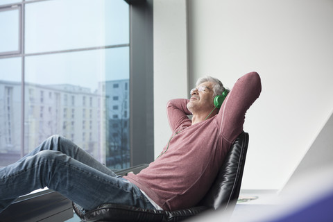 Mann sitzt in einem Ledersessel und hört Musik mit Kopfhörern, lizenzfreies Stockfoto