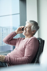 Man sitting in a leather chair telephoning with smartphone - RBF002624