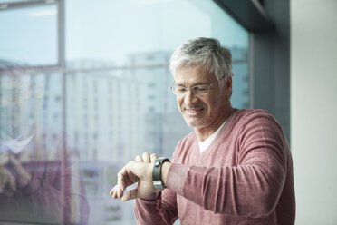 Lächelnder Mann schaut auf seine Smartwatch - RBF002628