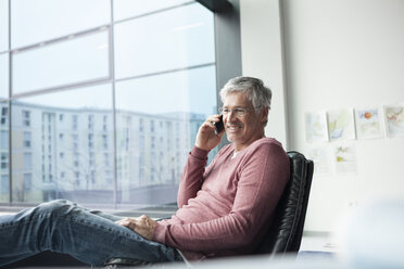 Mann sitzt in einem Ledersessel und telefoniert mit einem Smartphone - RBF002631