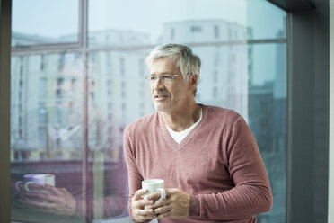 Porträt eines Mannes mit Kaffeetasse, der durch ein Fenster schaut - RBF002638