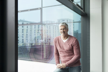 Porträt eines lächelnden Mannes mit grauem Haar vor einem Fenster - RBF002640