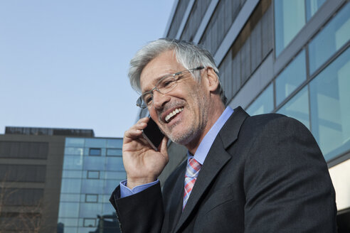Porträt eines lächelnden Geschäftsmannes, der mit einem Smartphone telefoniert - RBF002643