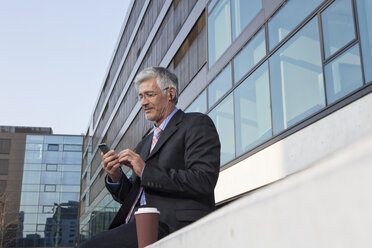 Smiling businessman hearing music with earphones - RBF002645