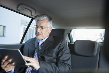 Geschäftsmann, der in einem Auto sitzt und ein digitales Tablet benutzt - RBF002647