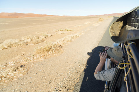 Namibia, Namib-Wüste, Namib Naukluft Park, Sossusvlei, Mann im Auto schaut durch ein Fernglas, lizenzfreies Stockfoto