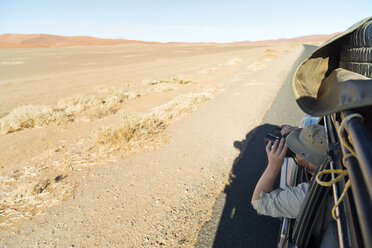 Namibia, Namib-Wüste, Namib Naukluft Park, Sossusvlei, Mann im Auto schaut durch ein Fernglas - CLPF000096