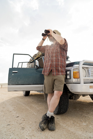 Namibia, Etosha-Nationalpark, Mann lehnt am Auto und schaut durch ein Fernglas, lizenzfreies Stockfoto