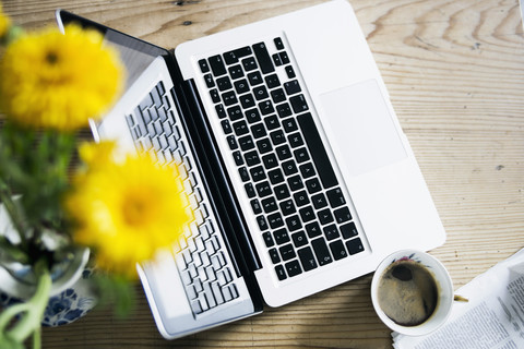 Tasse Kaffee, Blumen, Zeitung und Laptop auf Holz, lizenzfreies Stockfoto