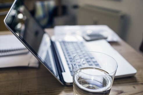 Glas Wasser, Dokumente und Laptop auf einem Holztisch - RIBF000005