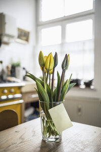 Klebezettel auf Glas mit Tulpen auf einem Küchentisch klebend - RIBF000021
