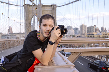 USA, New York, Porträt eines Reisenden mit Kamera auf der Brooklyn Bridge am Abend - GEMF000205