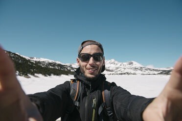 Spain, Catalonia, man taking a selfie in the mountains with frozen Lac des Bouillouses in the background - GEMF000211