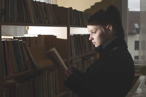 Studentin beim Lesen eines Buches in einer Bibliothek, lizenzfreies Stockfoto