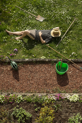 Mann liegt im Gras und entspannt sich bei der Gartenarbeit, lizenzfreies Stockfoto